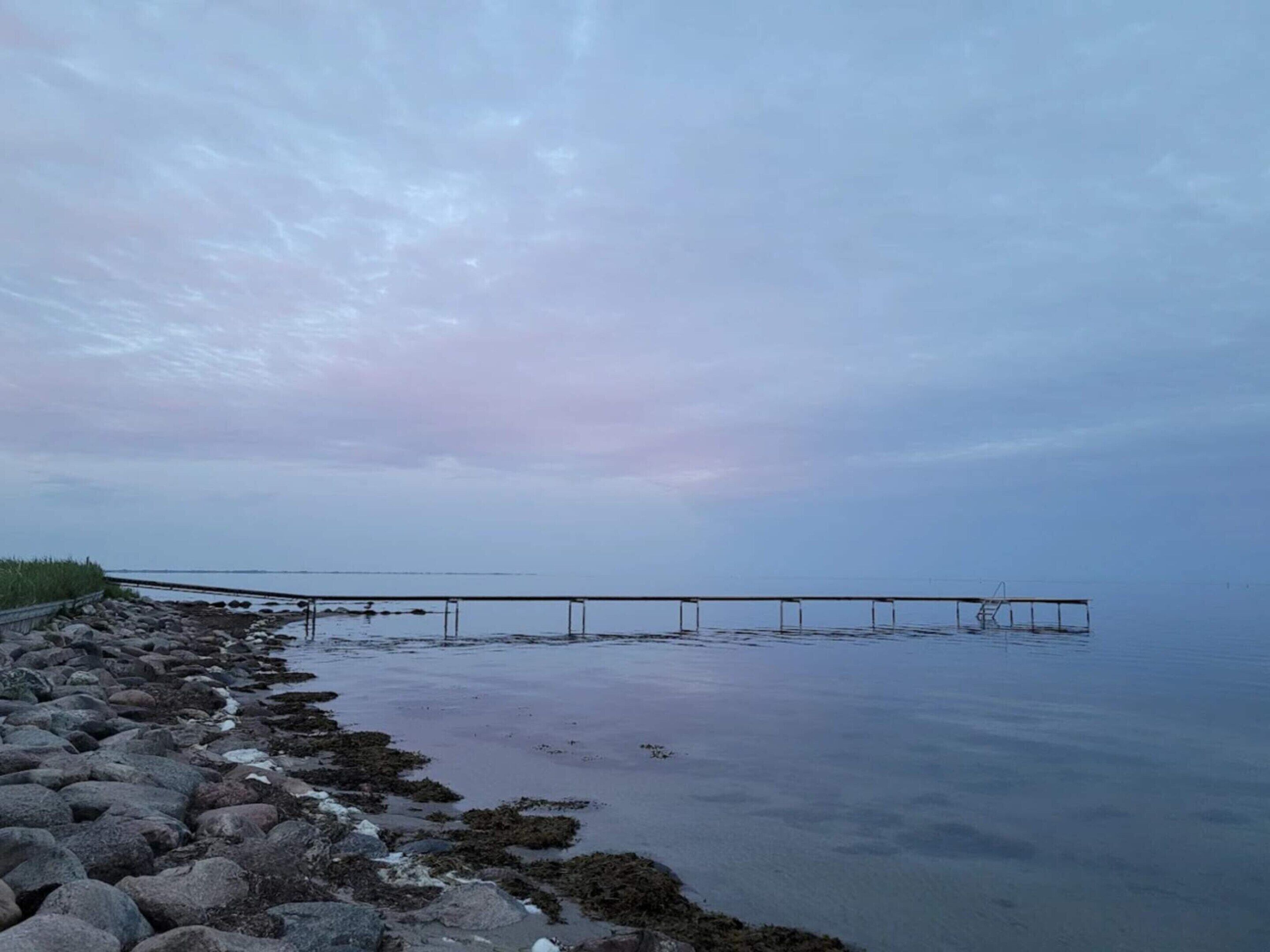 A rocky shoreline with a pier extending into calm waters.