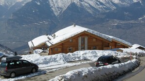 Een houten hut met een sneeuwbedekte kap, omringd door sneeuw, met een bergketen op de achtergrond.