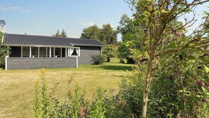 Une maison moderne, à l’extérieur gris et au toit en pente, entourée d’une pelouse bien entretenue et de diverses plantes.