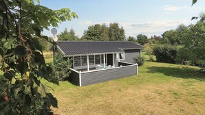 Une petite maison de plain-pied, avec un toit sombre et une grande véranda dotée de nombreuses fenêtres.