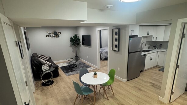 Een moderne keuken met witte kastjes en een roestvrijstalen koelkast. Er is een eethoek met een ronde tafel en twee stoelen.
