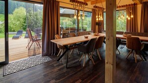 A spacious dining area with a wooden table and chairs, large windows with curtains, and a view of the outdoors. - Welcoming Villa With Amenities (Trutnov)