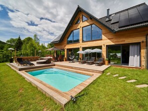 Ein modernes Holzhaus mit Pool, Sitzgelegenheit im Freien und großen Fenstern.