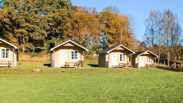 A row of small, single-story cabins with picnic tables in front, set in a grassy field with trees in the background. - Spacious Holiday Home in Hoor (Hoor)