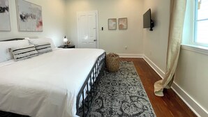 A bedroom with a bed, a nightstand, a wall-mounted TV, and a door. - Beautifully Restored! 3 Bedroom Home - 15 Min FQ! (New Orleans)