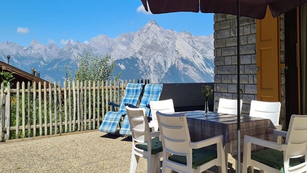 Un patio con tavolo e sedie, un ombrellone viola e vista sulle montagne innevate.
