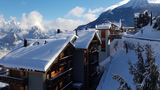 Un resort en la montaña cubierto de nieve, con edificios de madera y una vista despejada de las montañas.