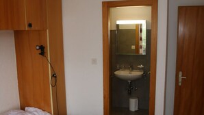 Un dormitorio con cama, armario de madera y baño visible a través de una puerta abierta.