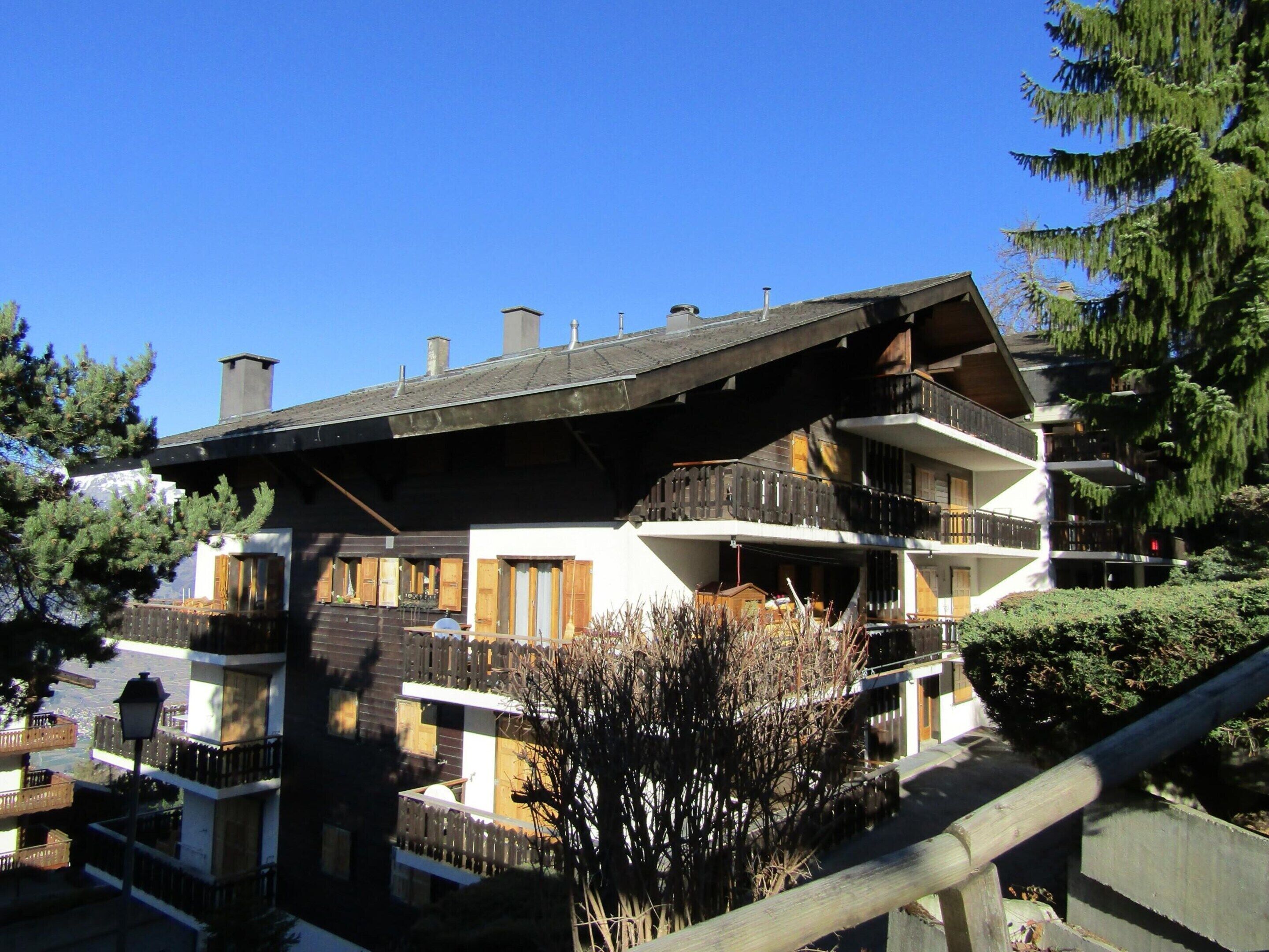 A multi-story building with balconies, wooden shutters, and a sloped roof.