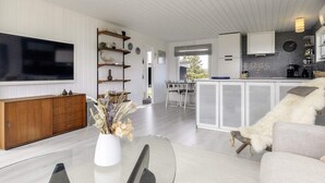 Una sala de estar moderna con un televisor de pantalla plana, un mueble de madera, una mesa de centro de cristal y un sofá blanco.