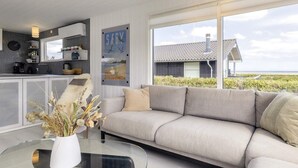 Una sala moderna con un sofá, una mesa de centro de vidrio y una zona de cocina con un ventanal.