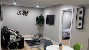 A modern living room with a round table, two chairs, a sofa, a TV, and a decorative wall piece. - Cozy 1BR Suite at Winnipeg South (Winnipeg)