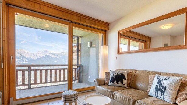 Una sala de estar acogedora con un sofá de cuero, una mesita redonda y vistas a montañas a través de un ventanal corredero.