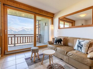 Un salon chaleureux avec un canapé en cuir, une petite table ronde et une vue sur les montagnes, visible à travers une porte-fenêtre coulissante.