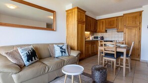 Un espacio habitable pequeño con sofá, una mesita redonda, un taburete, armarios de madera y un microondas.