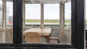 A covered outdoor seating area with a table and chairs, overlooking a grassy field. - 16 Person Holiday Home in Vestervig (Vestervig)