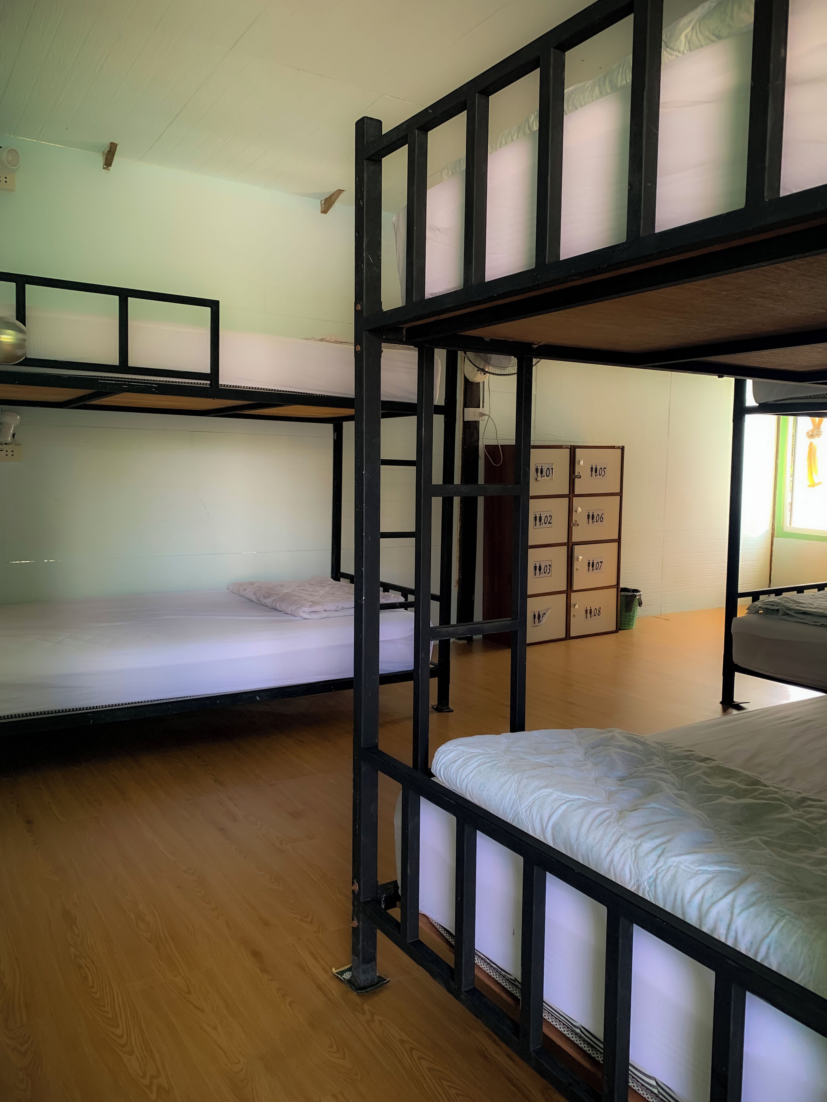 A dormitory room with bunk beds, a wooden floor, and a small storage unit with numbered compartments.