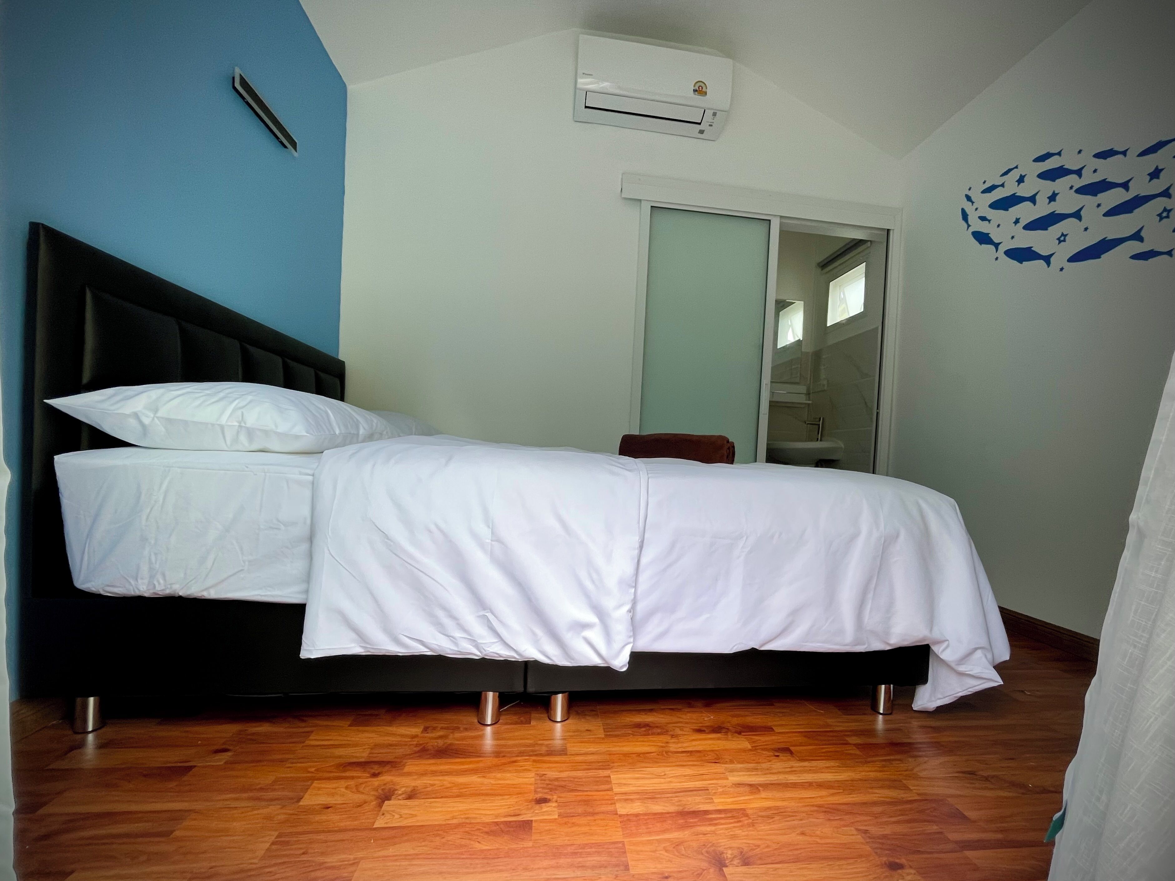 A bedroom with a bed, a wardrobe, an air conditioning unit, and a bathroom visible through a glass door.