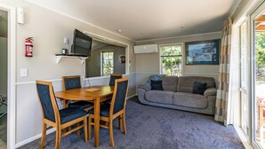 A room with a wooden dining table, four chairs, a grey sofa, and a television mounted on the wall. - Copper John, close to the Ski Fields here in the McKenzie. Quiet and private. (Middle Valley)