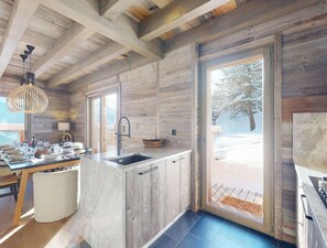 A modern kitchen with wooden walls, a large window, and a view of a snowy landscape. - Cosy Chalet in Vex With Balcony (Vex)