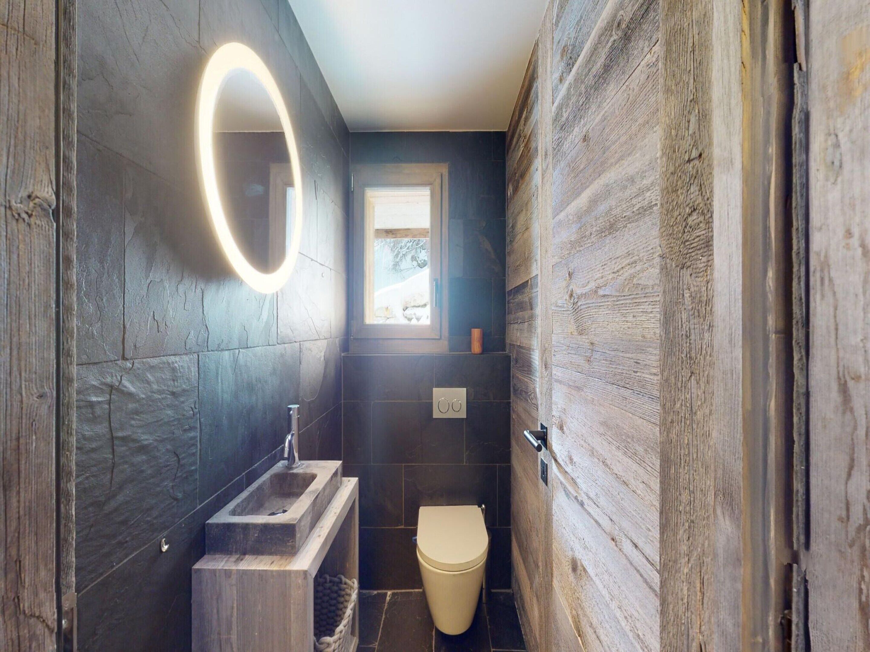 A compact bathroom with a wooden wall, a built-in sink, a toilet, and a small window.