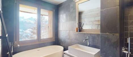 A modern bathroom with a freestanding bathtub, a large mirror, and a window with a view of mountains.