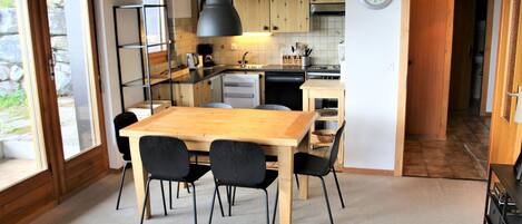 A modern kitchen with wooden cabinets, a dining table with chairs, and a clock on the wall.