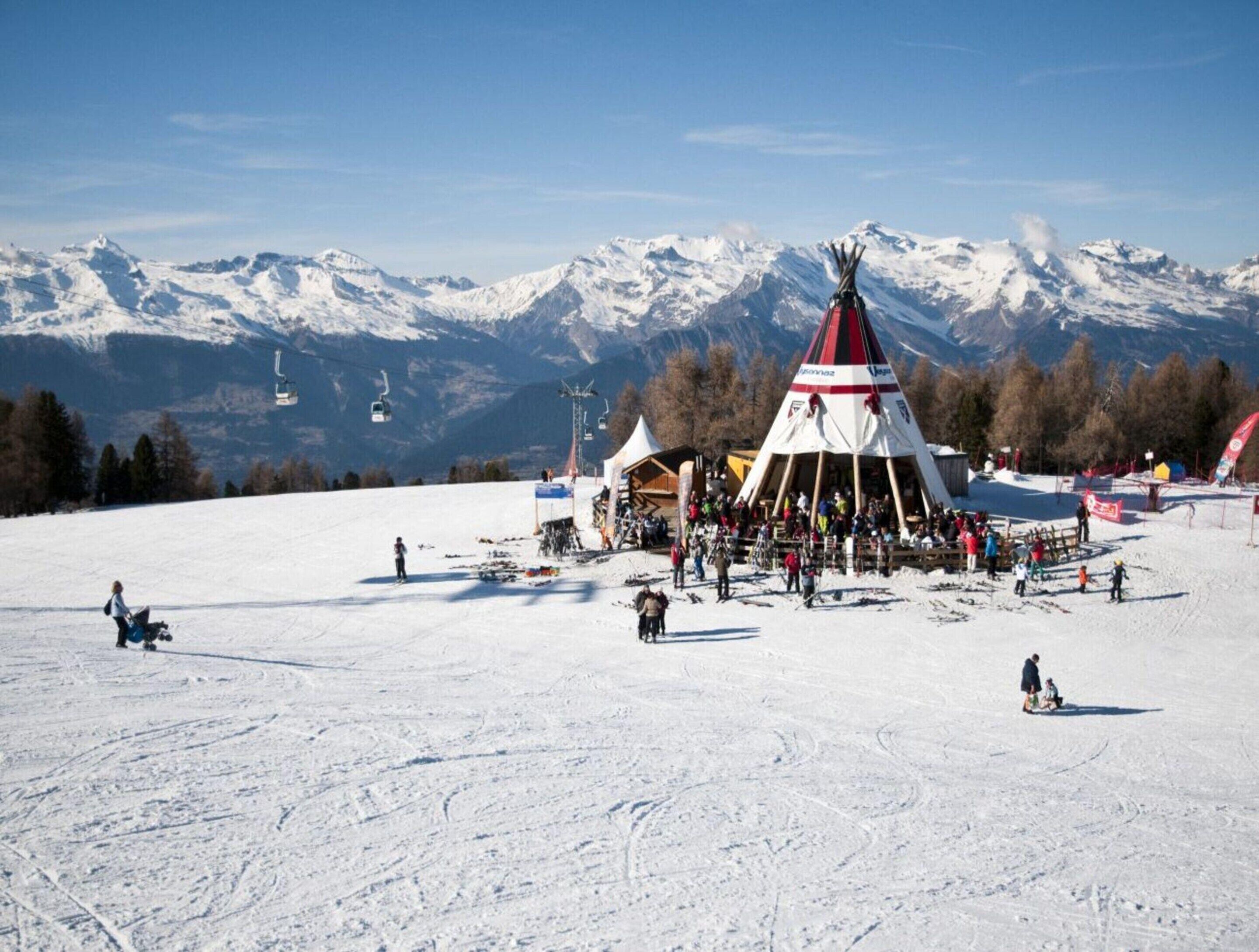 Une piste de ski enneigée, avec une grande structure en forme de tipi au centre, entourée de personnes et d'équipement de ski.