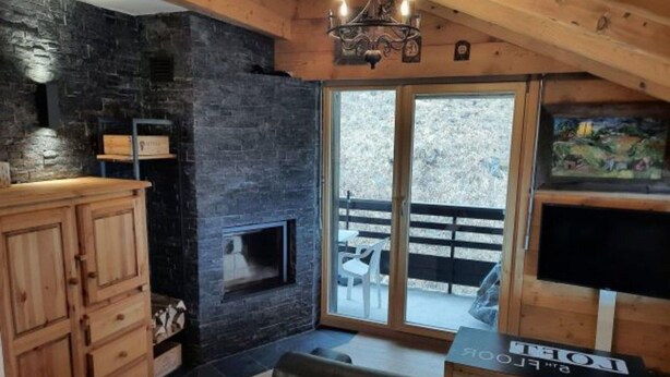 A cozy room with a stone fireplace, wooden cabinets, a black leather sofa, and a TV on a wooden stand. - Cozy Apartment With Rhone Valley View (Nendaz)