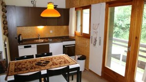 A compact kitchen with dark wooden cabinets, a white countertop, and a hanging orange pendant light. - Cozy Apartment With Rhone Valley View (Nendaz)