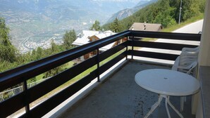Ein Balkon mit Blick auf ein Tal und Berge. Auf dem Balkon befinden sich ein Tisch und Stühle.