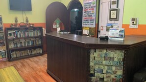 A reception desk with a wall-mounted TV, a bookshelf filled with books, and a wall displaying various service options like trekking, safari, and tours. - New Pokhara Lodge, Lakeside (Pokhara)