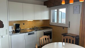 Et kompakt køkken med hvide skabe, en vask, en kogeplade og et vindue med udsigt.