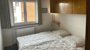 Et soveværelse med seng, træskab, et vindue med gardiner og en radiator.