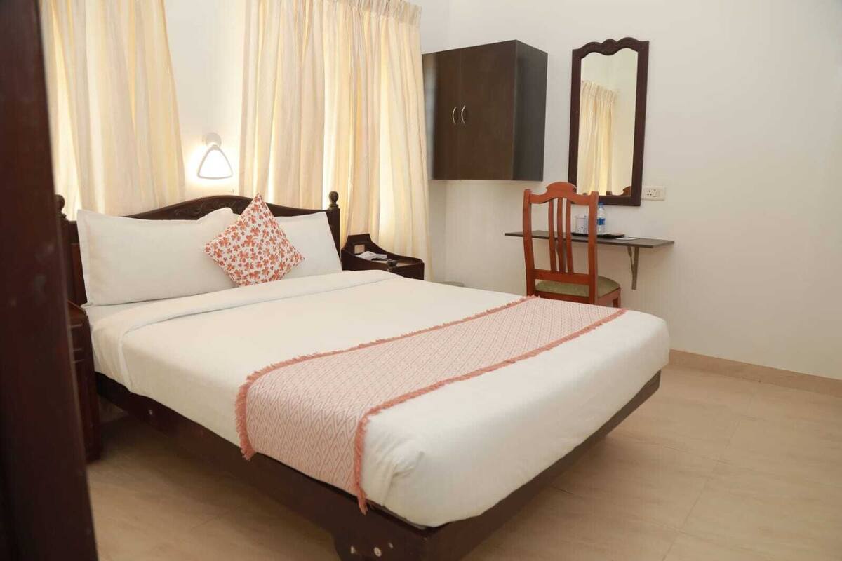 A neatly made bed with a patterned throw, a wooden nightstand, a chair, a wardrobe, and a mirror on the wall.