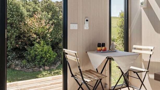 Et moderne værelse med store vinduer, et bord med stole og udsigt til grøn natur.