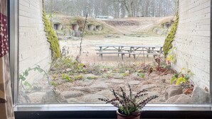 A view through a window of a courtyard with a wooden bench, potted plants, and a stone wall. - Scenic Holiday Home in Hoor (Hoor)