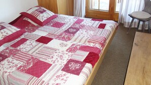 A bedroom with a bed, a wooden nightstand, a chair, and a window with curtains. - Trendy Apartment in the Heart of Hills (Sion)