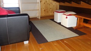 A cozy attic room with a wooden ceiling, a black leather sofa, two white ottomans with red pillows, and a wooden table. - Trendy Apartment in the Heart of Hills (Sion)