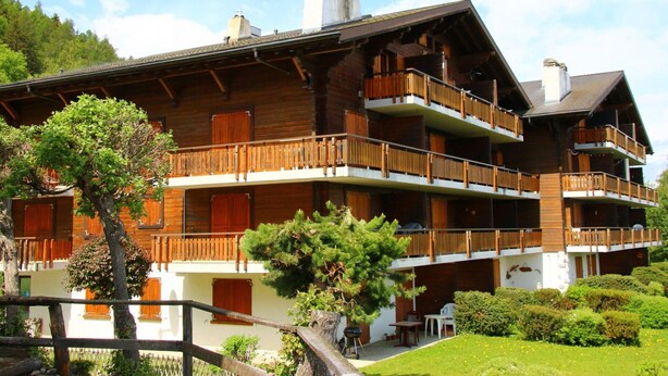 A multi-story wooden chalet with balconies, surrounded by lush greenery and a clear sky. - Trendy Apartment in the Heart of Hills (Sion)