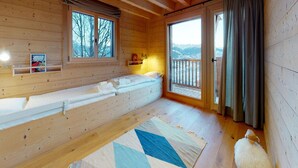 Ein gemütliches Blockhauszimmer mit Holzvertäfelung, einem großen Fenster mit Bergblick, einer Bank mit Kissen und einem Hund.