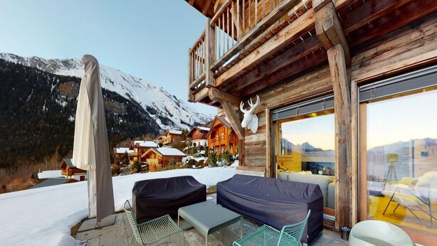 Eine Holzchalet mit einem Balkon mit Blick auf eine verschneite Berglandschaft.