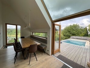Zona pranzo moderna con tavolo e sedie in legno, ampie finestre e vista su una piscina.