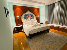 Un dormitorio con una cama grande, un cabecero decorativo, lámparas de noche, una ventana con cortinas y una alfombra estampada.