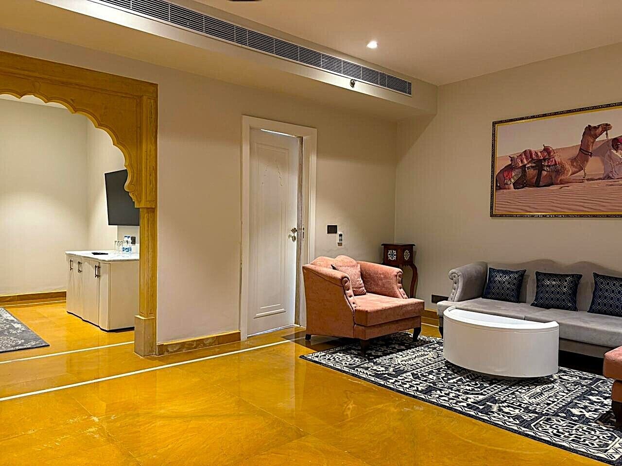 Uma sala de estar moderna com um sofá, poltrona e um banquinho, um tapete estampado e um quadro na parede.