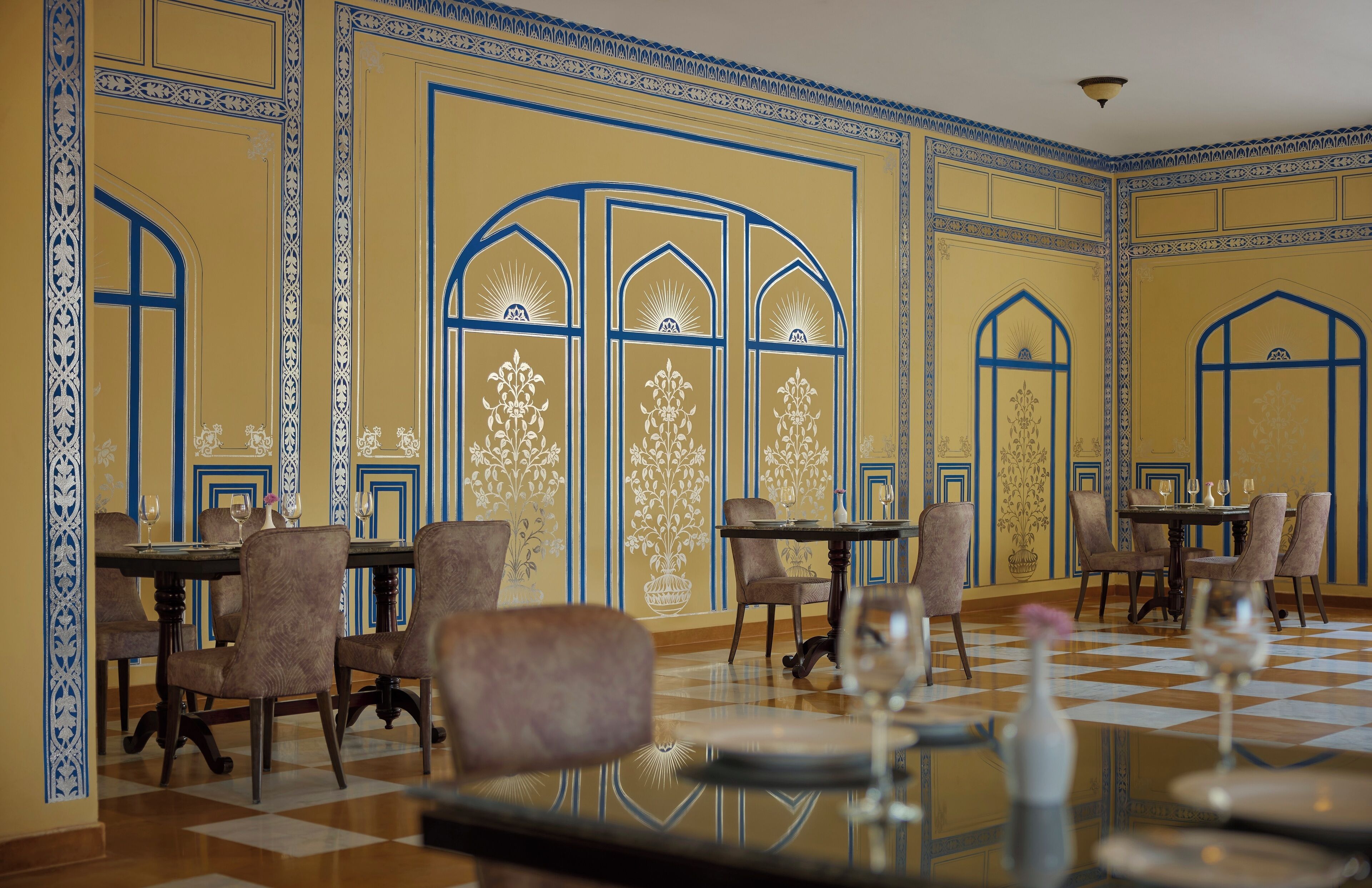 A dining area with checkered flooring, tables with chairs, and decorative wall patterns.