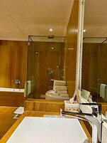 Un baño moderno con ducha envuelta en vidrio, tocador de madera y un espejo grande.