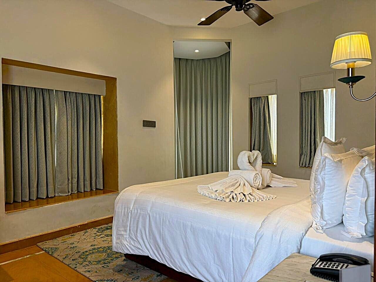 A hotel room with a large bed, a ceiling fan, a bedside telephone, and a window with curtains.