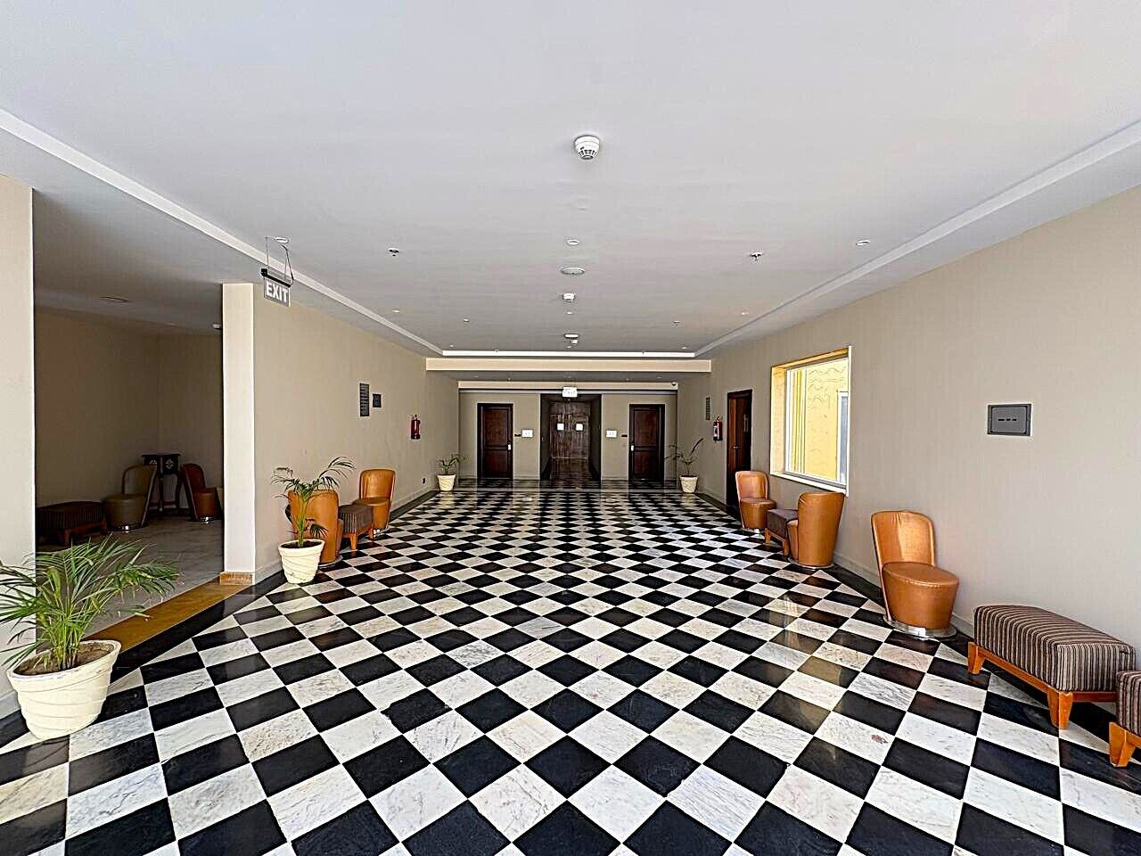 A hotel lobby with a checkered floor, a reception desk, and seating areas.