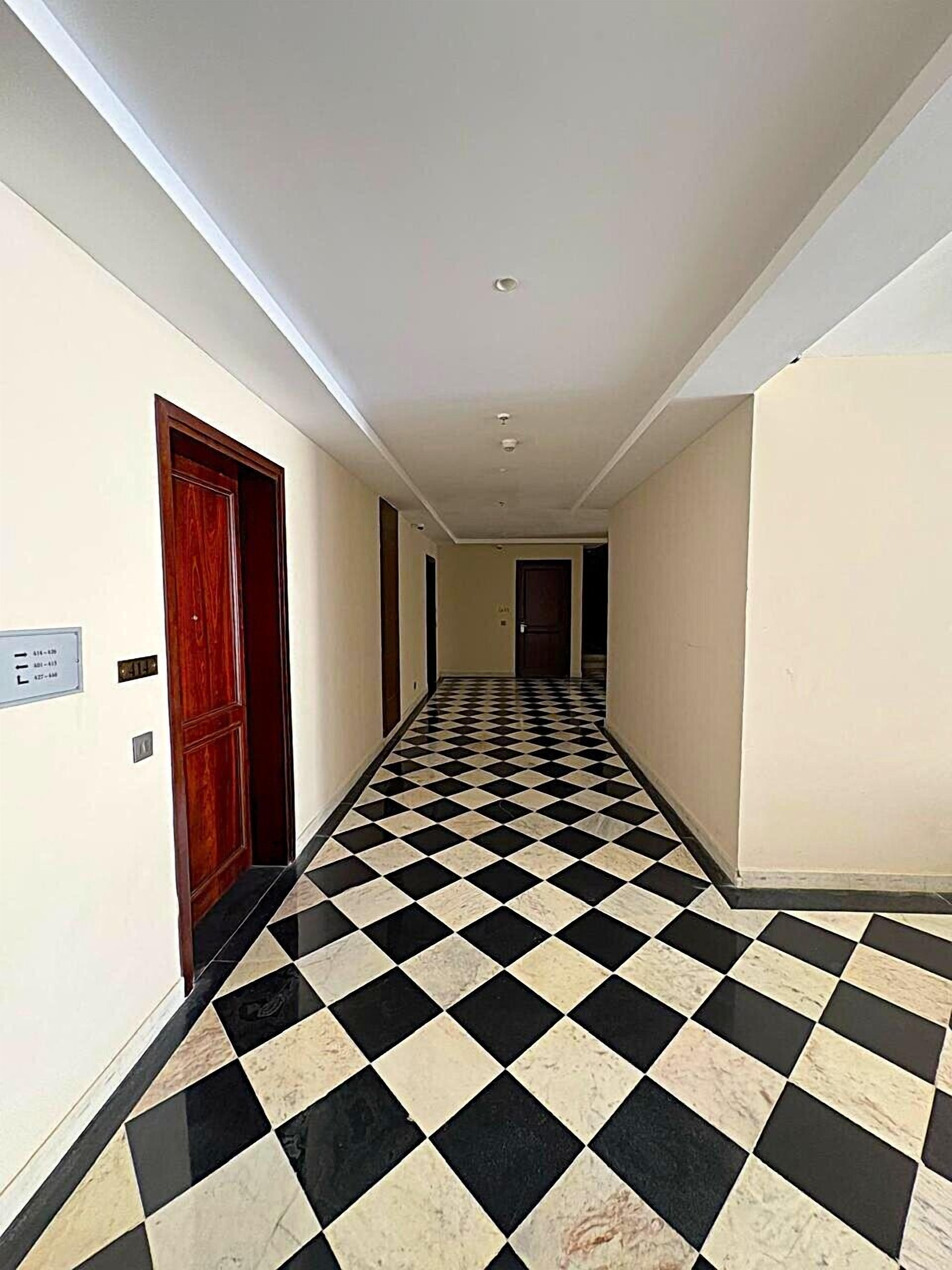 A hallway with a black and white checkered floor, white walls, and a wooden door on the left.